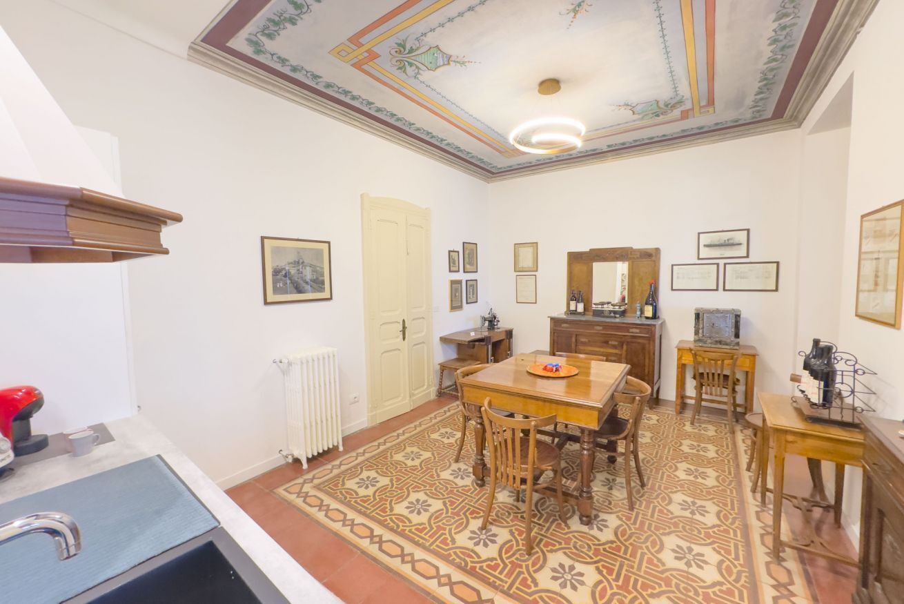 Een eetruimte met een houten tafel, stoelen, een kamerkleed met dessin en een plafond met decoratieve details.