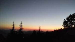 Eine Berglandschaft im Abendrot mit schattensilhouetten von Bäumen und einem klaren Himmel.