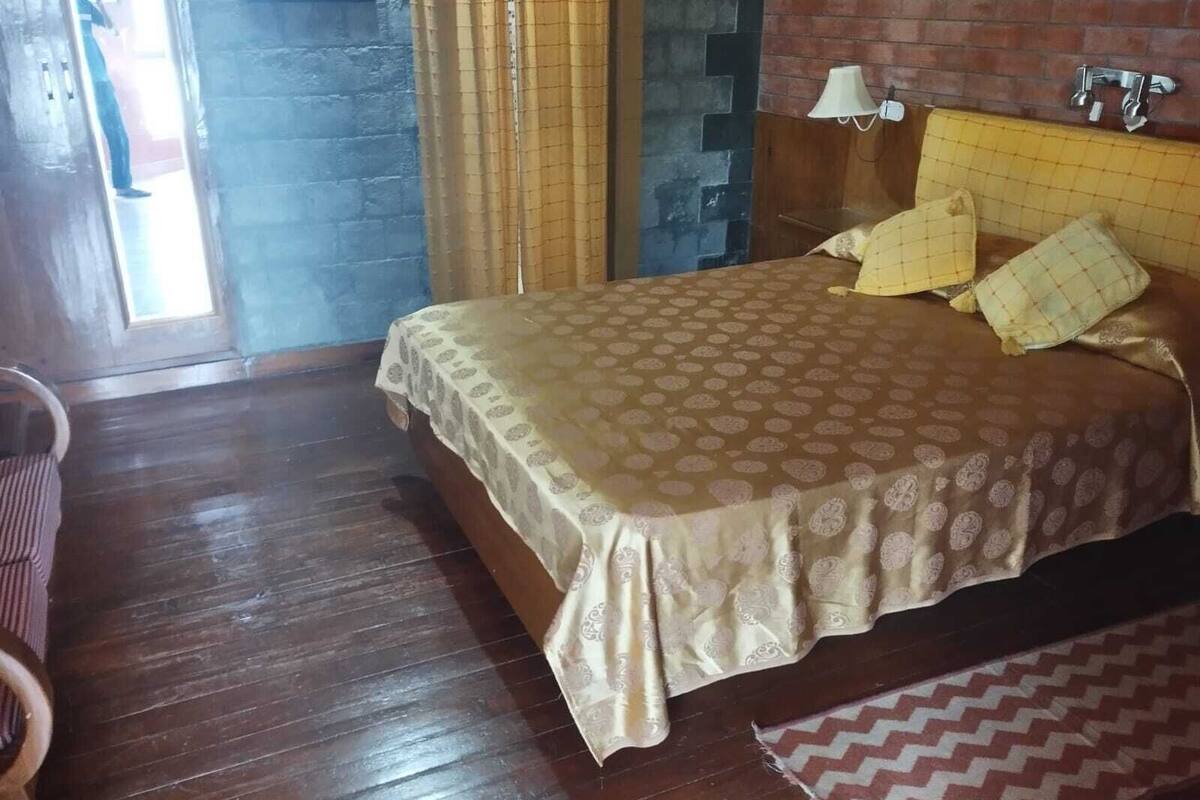 Ein Schlafzimmer mit Bett, Holzboden, Vorhängen, einer Lampe und einer Ziegelwand.
