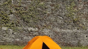 A tent set up on a grassy field with a stone wall in the background. - Himgiri Nature Retreat (Rajgarh)