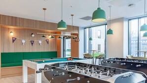 A modern indoor recreation area with foosball tables, a pool table, and green seating. - For Students Only - Straits Meadow in Edinburgh City Centre - Campus Accommodation (Edinburgh)
