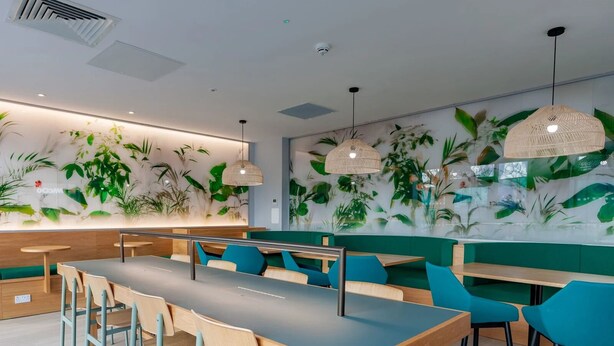A modern restaurant interior with long communal tables, blue and wooden chairs, and green cushioned seating. - For Students Only - Straits Meadow in Edinburgh City Centre - Campus Accommodation (Edinburgh)