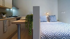 A compact room with a kitchenette, a bed with patterned bedding, and a potted plant. - For Students Only - Straits Meadow in Edinburgh City Centre - Campus Accommodation (Edinburgh)