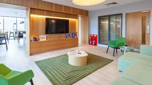 A modern living room with a large flat-screen TV, wooden paneling, green chairs, a round coffee table, and a green rug. - For Students Only - Straits Meadow in Edinburgh City Centre - Campus Accommodation (Edinburgh)