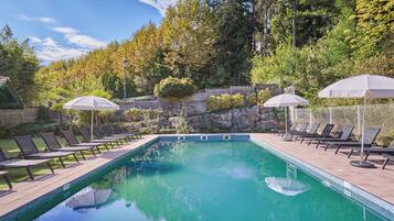 A rectangular swimming pool with a tiled edge, surrounded by lounge chairs and umbrellas.