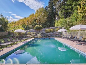 Une piscine rectangulaire dont le bord est recouvert de carreaux, entourée de chaises longues et de parasols.