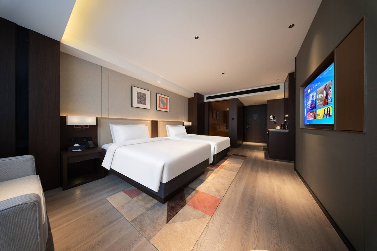 A modern hotel room with a large bed, bedside tables, a flat-screen TV, and a wooden floor.