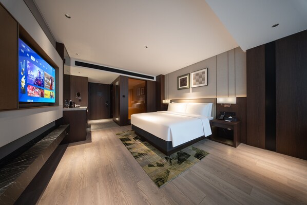 Una habitación de hotel moderna con una cama grande, un televisor montado en la pared, un escritorio con una silla y una mesita de noche con una lámpara.