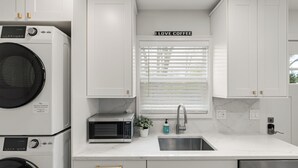 A modern kitchen with white cabinetry, a built-in microwave, a stainless steel sink, and a window with blinds.