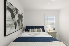 A bedroom with a large bed, a world map artwork on the wall, a bedside table with a lamp, and a window with blinds. - Modern Retreat in the Heart of Royal Oak (Royal Oak)