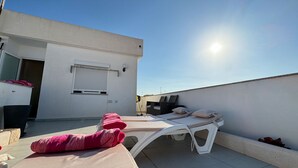 Une terrasse sur le toit avec un transat, une petite table et une chaise.
