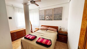 Une chambre à coucher comprenant un lit, des tables de chevet, une commode, un ventilateur de plafond et des œuvres d’art accrochées au mur.