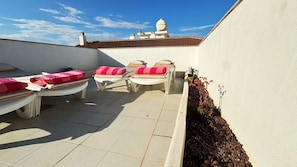 A rooftop terrace with sun loungers, a small garden, and a white building with a tiled roof in the background. - Low Price Modern Apartment, Aircon & Filter Water (San Pedro del Pinatar)