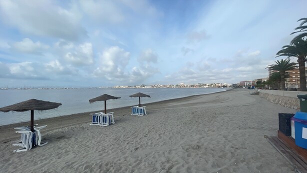 Une plage avec des parasols et des chaises longues, un mur de pierre et une vue sur la mer et les bâtiments au loin.