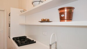 Cucina con mobili bianchi, piano cottura nero, lavello bianco e pentole di rame sugli scaffali.
