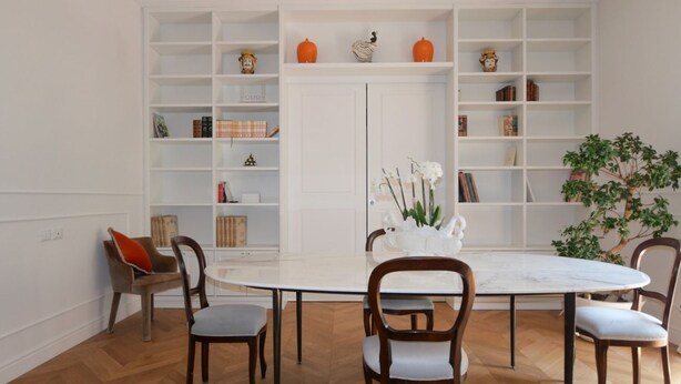 Zona pranzo con tavolo rotondo, sei sedie e una libreria bianca con oggetti decorativi.