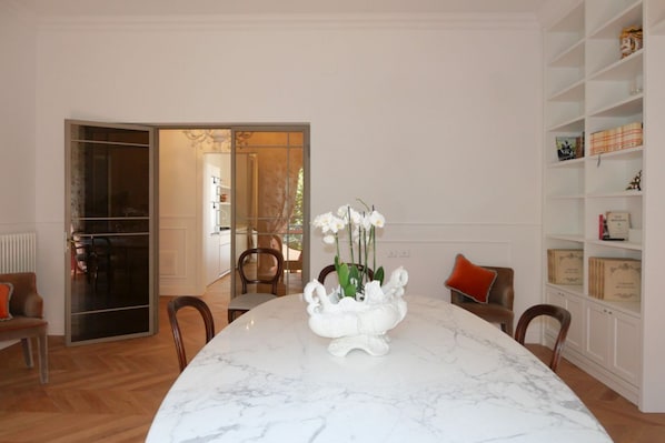 Un coin repas avec une table en marbre, des chaises et un vase rempli de fleurs blanches. On y trouve également une bibliothèque avec des livres et des objets décoratifs.