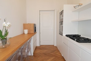 Une cuisine moderne avec des meubles blancs, un plan de travail en bois, une porte blanche et une cuisinière.