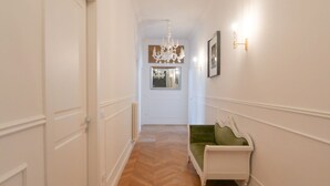Un corridoio con pavimento a spina di pesce, una porta bianca, un divano imbottito verde, un lampadario e un quadro appeso al muro.