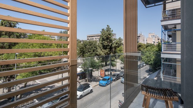 Een balkon met houten lamellen, uitzicht op een straat met geparkeerde auto's en gebouwen op de achtergrond.