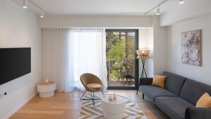 Een moderne woonkamer met een bank, een fauteuil, een televisie en een groot raam met gordijnen.