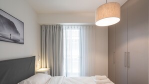 Een moderne hotelkamer met een groot bed, nachtkastje, kledingkast en een raam met gordijnen.
