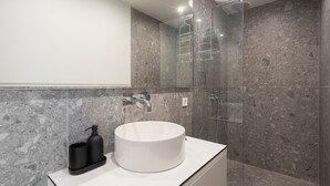 A modern bathroom with a round white sink, a black soap dispenser, and a glass shower enclosure. - LIV Athinum 1 - Luxury Apartment 3B (Athens)