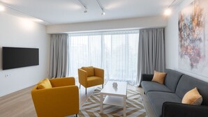 A modern living room with a sofa, two armchairs, a coffee table, and a flat-screen TV mounted on the wall. - LIV Athinum 1 - Luxury Apartment 3B (Athens)