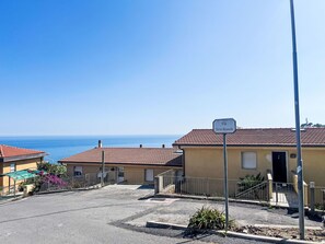 A residential street with a clear view of the sea, a sign reading "Via Terre Bianche", and a building with a tiled roof.