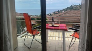 Een balkon met een tafel voor twee, uitkijkend op een kustlandschap.