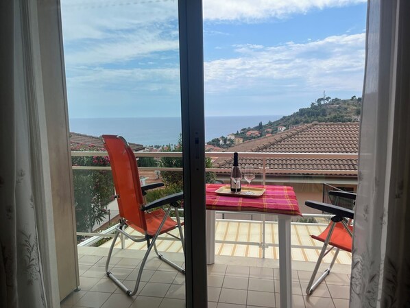 Un balcón con una mesa lista para dos personas, con vistas a un paisaje costero.