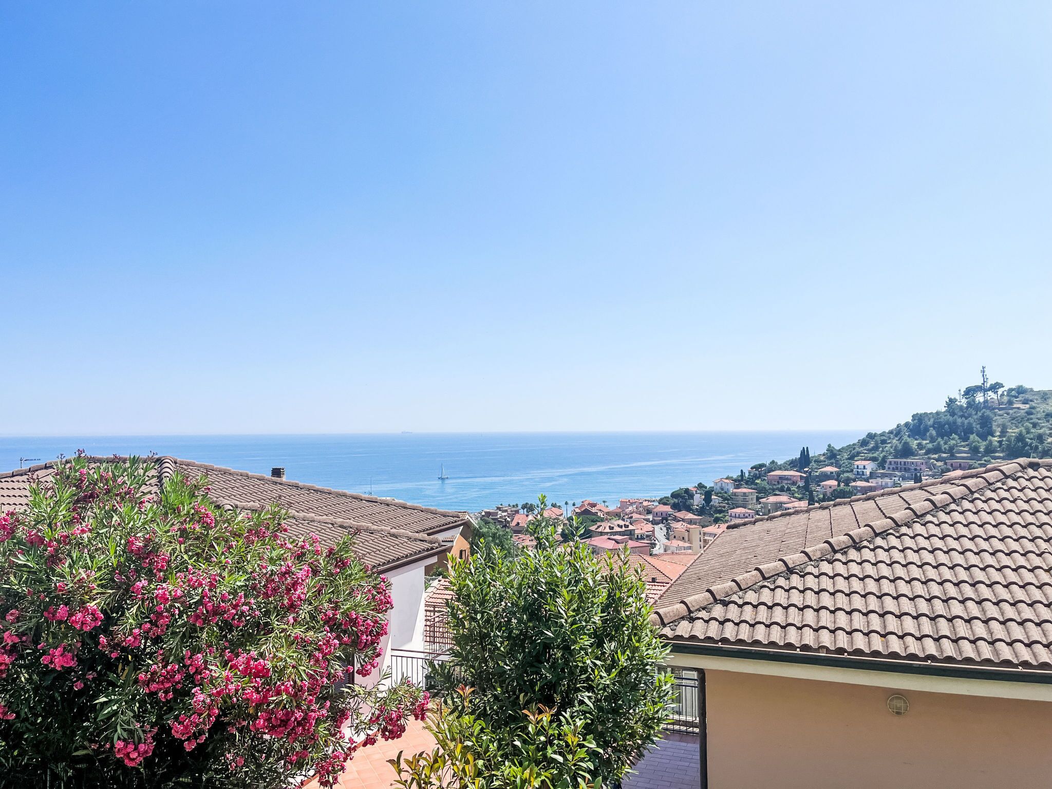A coastal town with terracotta-roofed buildings, a clear blue sky, and a view of the sea.