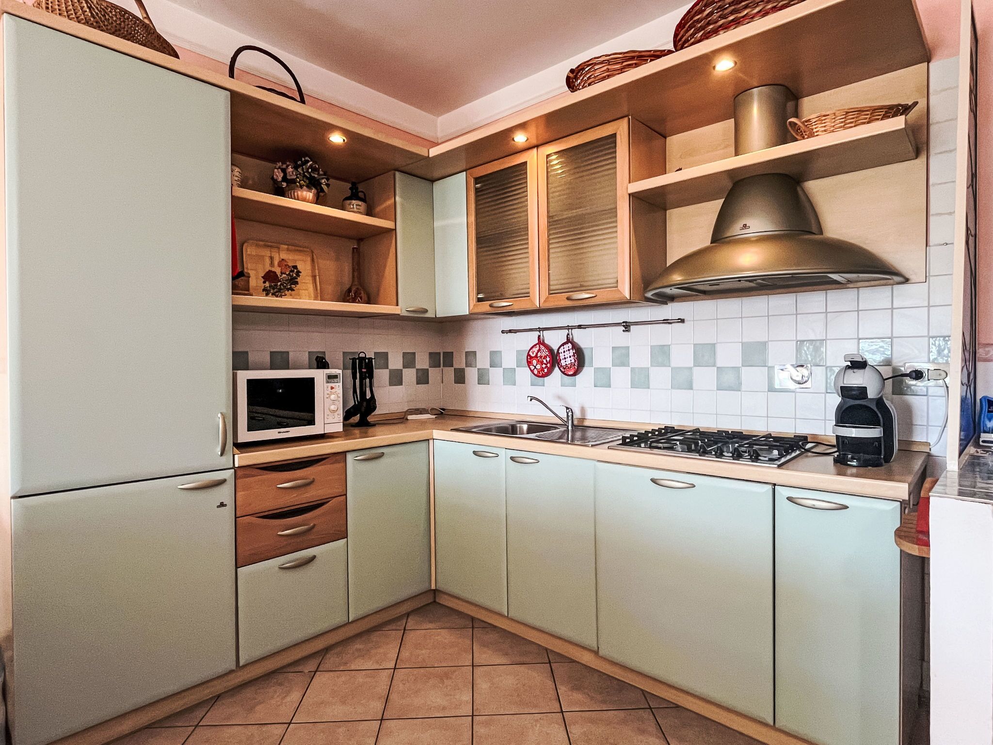A kitchen with light green cabinets, a white microwave, a gas stove, and a coffee maker.