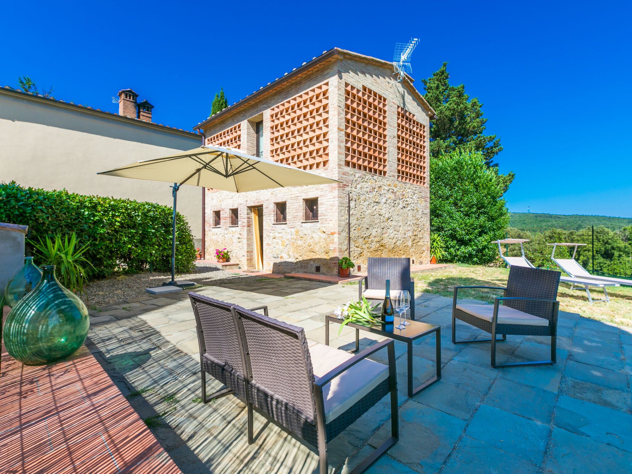 Un patio con mobiliario exterior, un edificio de piedra con chimenea y un cielo azul despejado.