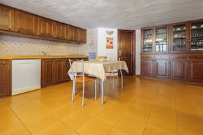 Una cocina con armarios de madera, lavavajillas, mesa de comedor con sillas y piso de baldosas.
