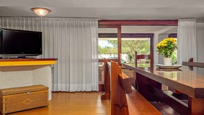A room with a television, wicker furniture, a bench, a table with a vase, and a view through a glass door. - Holiday Villa for Complete Relaxation (Olbia)