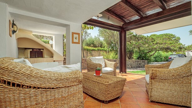 A covered outdoor seating area with wicker furniture and a view of the garden. - Holiday Villa for Complete Relaxation (Olbia)