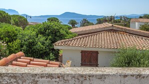 A coastal building with a tiled roof, a wooden door, and a view of the sea and mountains in the background. - Holiday Villa for Complete Relaxation (Olbia)