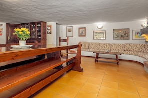 Un comedor con mesa de madera, bancos, un sofá y un armario.