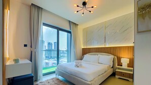 A modern hotel room with a large bed, a nightstand, a lamp, a marble wall, and a view of a cityscape through a large window.