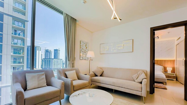 A modern living room with a sofa, armchairs, a coffee table, and a view of high-rise buildings.