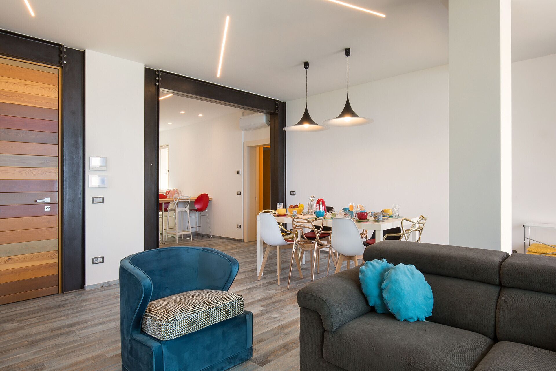 Een moderne woonkamer met een bank, een blauwe fauteuil en een eethoek met een tafel en stoelen.