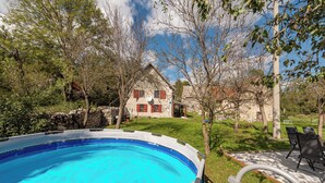 An outdoor swimming pool with a stone wall and a house in the background. - 4-bedroom house in charming Gračac with WiFi (Gračac)