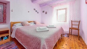 A bedroom with a bed, pillows, a chair, a wooden floor, a window with curtains, and a shelf with a bag. - 4-bedroom house in charming Gračac with WiFi (Gračac)