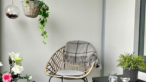 A room with a wicker chair, a small table with a potted plant, a hanging plant, and a glass vase with flowers. - Twin with city views (Helsinki)