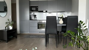 A modern kitchen with grey cabinets, a built-in oven, and a dining area with black chairs and a wooden table. - Twin with city views (Helsinki)