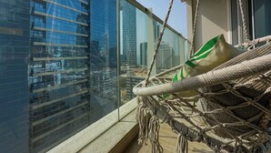 Un balcon donnant sur un paysage urbain, un hamac et une fenêtre offrant une vue sur de hauts immeubles.