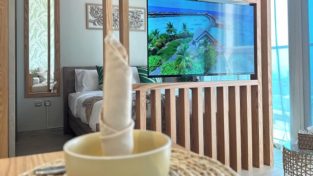 Une chambre moderne équipée d’un lit, d’un téléviseur diffusant des images de paysages tropicaux et d’une cloison en bois.