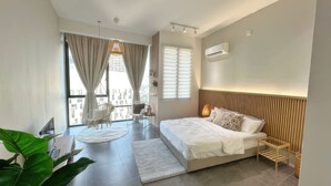 Un dormitorio moderno con una cama grande, una mesita pequeña, una silla y vistas a edificios a través de amplios ventanales.