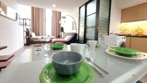 Una cocina moderna con una isla central, un área de comedor con mesa de vidrio y una sala de estar con sofá y cortinas.